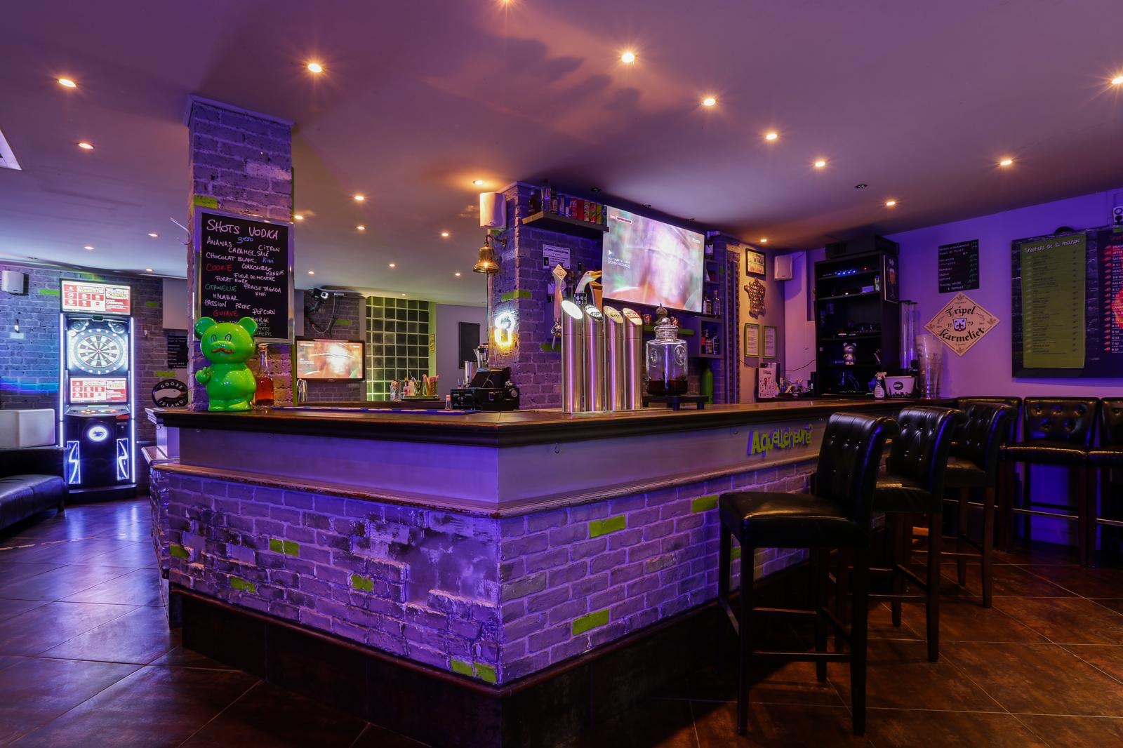 Comptoir du bar sous lumière violette, tireuses et ours vert